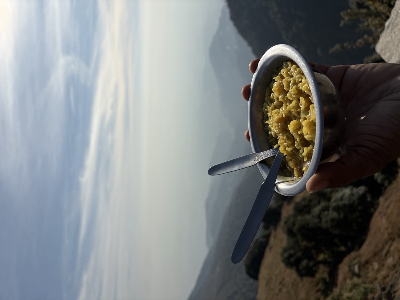 A bowl of hot Maggi held against the mountain valley view