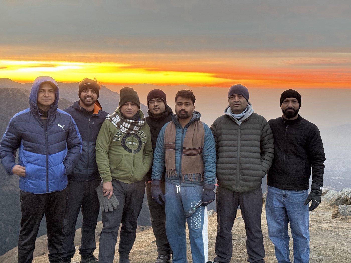 All seven friends standing together in front of a bright orange Triund sunrise
