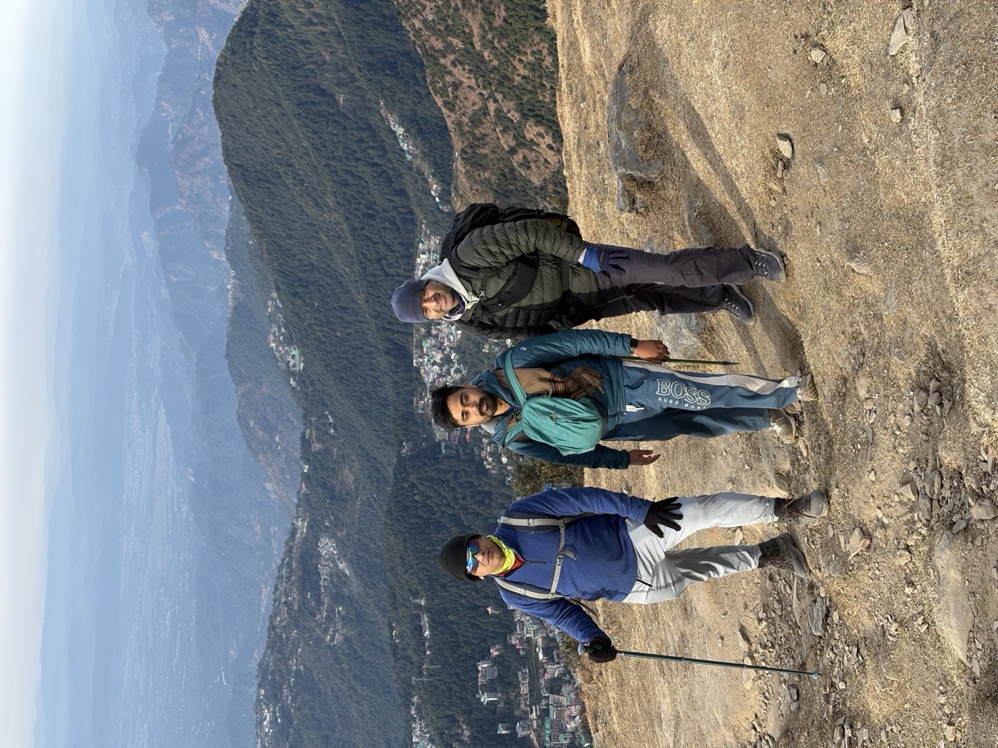 Three friends paused on the descending trail with Dharamshala visible below