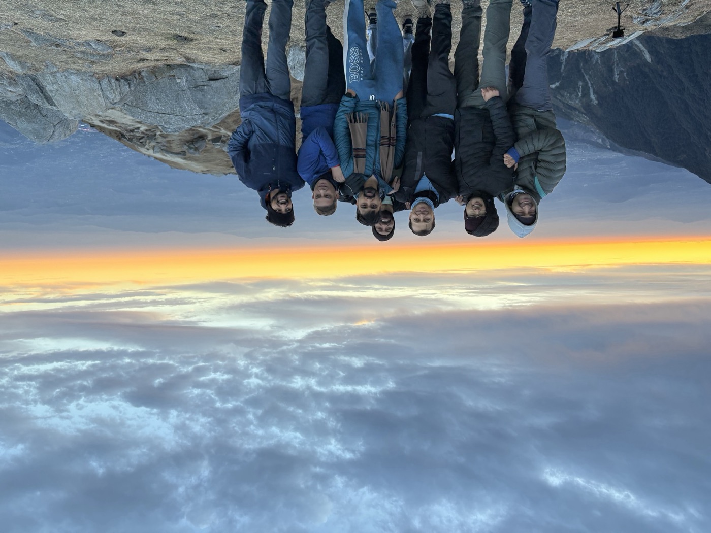 The seven friends standing close together above the valley at sunrise before descending